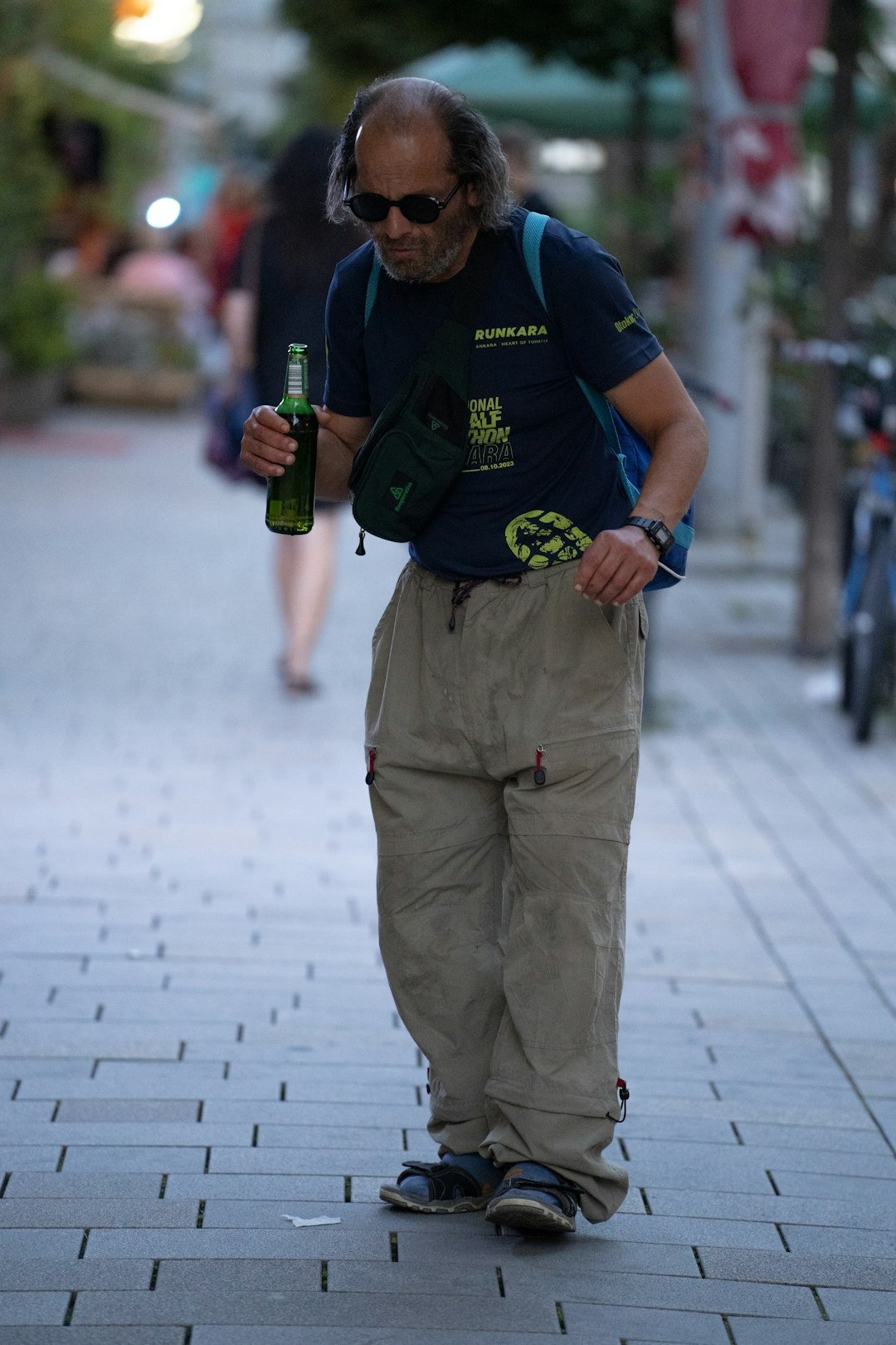 Man walking on a sidewalk carrying a bag and bottle.