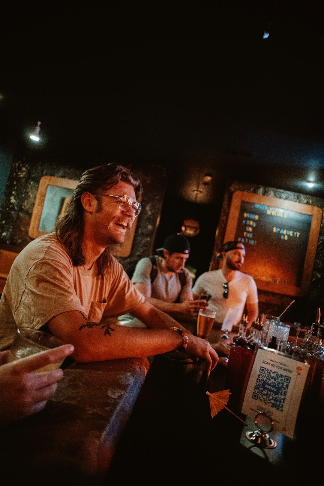 Three men socialize while sitting at a wooden bar counter.
